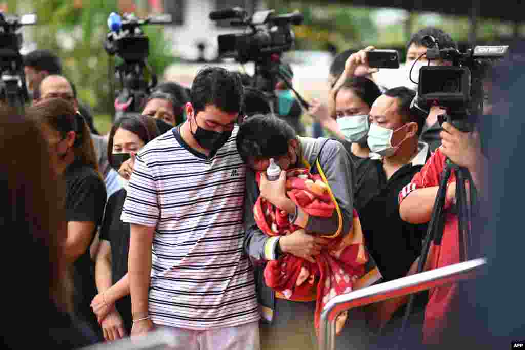 Sittipong Taothawong, left, comforts his wife Kanjana Buakumchan as she holds their child's milk bottle and blanket while standing outside the nursery in Na Klang in Thailand's northeastern Nong Bua Lam Phu province, the day after a former police officer killed at least 37 people in a mass shooting at the site.