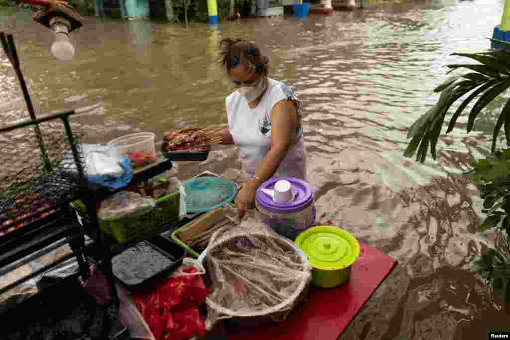 A woman prepares barbecue to sell along a flooded street following heavy rains brought by tropical storm Nalgae, in Imus, Cavite province, Philippines.