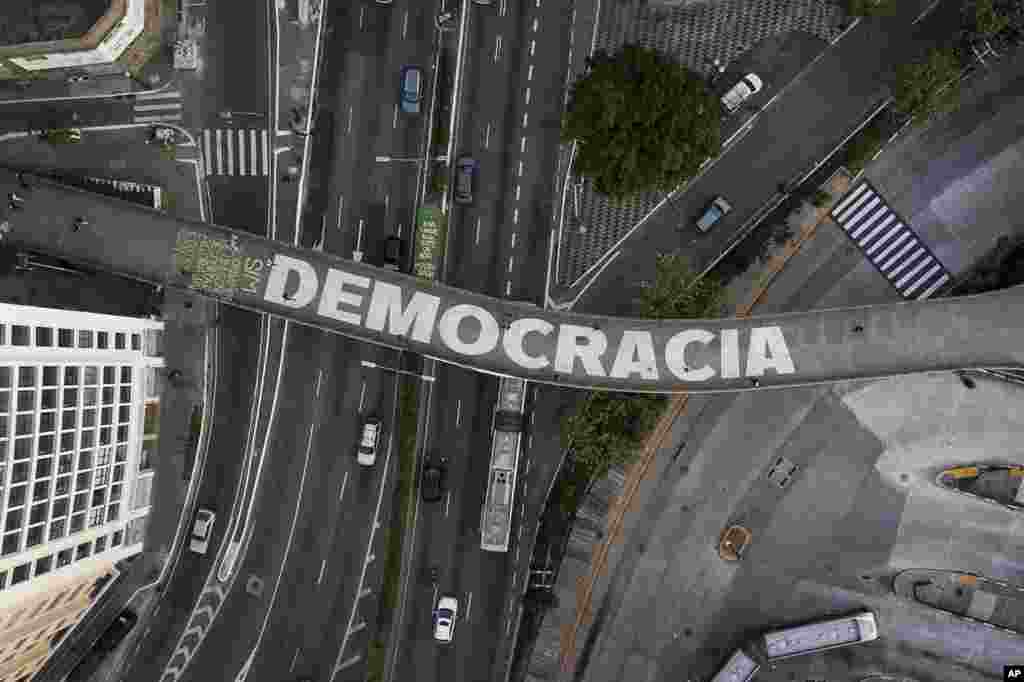 People walk on a pedestrian bridge that has written "Democracy" in Portuguese in Sao Paulo, Brazil, Oct. 26, 2022.