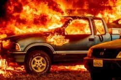 Flames from the Dixie Fire consume a pickup truck on Highway 89 south of Greenville on Aug. 5, 2021, in Plumas County, Calif.
