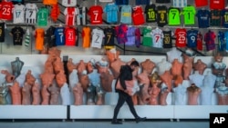 A shop clerk carries mannequins at a soccer jerseys stand at a tourist shopping area, in Belek, Antalya, Turkey, Saturday, March 12, 2022. After losing two years to the COVID-19 pandemic, shopkeepers in the heart of the Turkish Riviera had hoped for a str