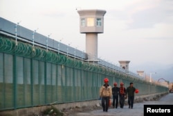 FILE - Workers walk by the perimeter fence of what is officially known as a vocational skills education center in Dabancheng in Xinjiang Uighur Autonomous Region, China, Sept. 4, 2018.