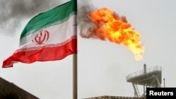 FILE - A gas flare on an oil production platform in the Soroush oil fields is seen alongside an Iranian flag in the Persian Gulf, Iran, July 25, 2005.