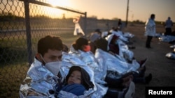 Migrantes centroamericanos con niños esperan en un campo de béisbol después de cruzar el Río Grande hacia EE. UU. en balsas, en La Joya, Texas, el 19 de marzo de 2021.