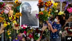 Flowers are placed on a fence surround a portrait of former Anglican Archbishop Desmond Tutu outside St. George's Cathedral in Cape Town, South Africa, Dec. 27, 2021. At midday bells are rung to honor Tutu, a day after his death. (AP Photo)