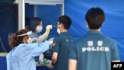 Medical workers in a booth take test samples for the COVID-19 coronavirus from South Korean police officers at Seoul Metropolitan Police Agency's maneuver headquarters in Seoul on August 19, 2020. - All police officers who were on duty during a rally on t