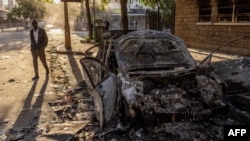 Um homem passa pelos destroços de um carro incendiado por manifestantes na sequência de uma greve mortal a nível nacional para protestar contra o aumento dos impostos e a Lei das Finanças de 2024 no centro de Nairobi, 26 de junho de 2024.