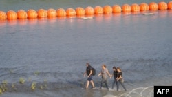 Wahamiaji wakitembea karibu na uzio wa waya kwenye mpaka wa Marekani na Mexico wa Rio Grande .July 16, 2023.