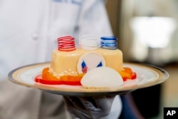 White House executive pastry chef Susie Morrison, right, holds a dish during a media preview for the State Dinner with President Joe Biden and French President Emmanuel Macron in the State Dining Room of the White House in Washington, Wednesday, Nov. 30, 2022. The dinner will include a butter poached Maine lobster, beef with shallot marmalade, American artisanal cheeses, and an orange chiffon cake for desert. (AP Photo/Andrew Harnik)