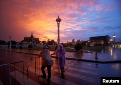 FILE - Men stand in front of the Royal Palace in Phnom Penh, Cambodia. Analysts say Cambodia’s lax regulatory environment and tax loopholes mean the scale of offshoring and its economic impact on the Southeast Asian country remain unknown.