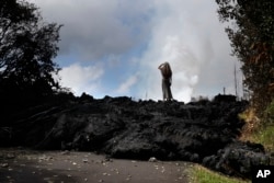 Hannique Ruder, 65, a resident of the Leilani Estates subdivision, stands on a mound of hardened lava near Pahoa, Hawaii, May 11, 2018. The Kilauea volcano has destroyed more than 35 structures since it began releasing lava from vents about 25 miles (40 kilometers) east of the summit crater.