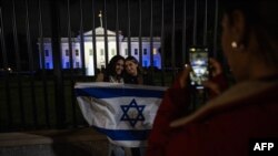 白宮2023年10月9日晚亮出以色列國旗的燈光，支持者們在大門前留影。（法新社）