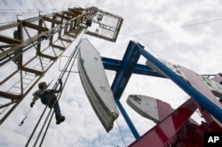 FILE - A worker hangs from an oil derrick outside Williston, N.D., where oil is taken from the Bakken shale formation.