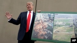 President Donald Trump holds a photo of the border area as he reviews border wall prototypes, March 13, 2018, in San Diego.