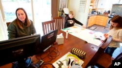 In this March 17, 2020 photo from Beaverton, Oregon, Kim Borton works from home while her children Logan, center, age 6 and Katie, age 7, as they work on an art project.