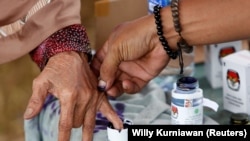 Seorang petugas pemilu membantu seorang perempuan lanjut usia untuk menandai jarinya dengan tinta setelah memberikan suaranya pada pilkada di Tangerang, Banten, 27 Juni 2018. (Foto: REUTERS/Willy Kurniawan)