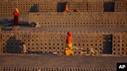 Women laborer transport bricks on hand carts at a brick kiln factory on the outskirts of Jammu, India, Nov. 26, 2013.