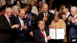 President Donald Trump shows the signed executive order surrounded by cabinet members and supporters in Miami, Friday, June 16, 2017