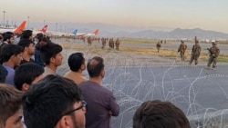 ប្រជាជន​អាហ្វហ្កានីស្ថាន (ឆ្វេង) កំពុង​ស្ថិតនៅ​អាកាសយានដ្ឋាន​ក្នុង​រដ្ឋធានី​កាប៊ុល ខណៈ​ដែល​ទាហាន​សហរដ្ឋ​អាមេរិក​ឈរ​យាម​ល្បាត នៅ​ថ្ងៃ​ច័ន្ទ​ ទី១៦ ខែសីហា ឆ្នាំ២០២១។