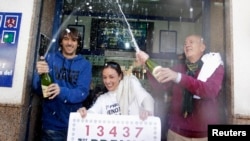 Lottery seller Raquel Carrasco (C) holds a sign with the winning number of Spain's Christmas Lottery "El Gordo", as employees spray champagne in La Eliana near Valencia December 22, 2014. The total prize money of 2.4 billion euros is split into thousands