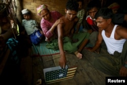 FILE - Abdhulami, center, 22, who was released from a human trafficking boat, points at pictures of people he recognises from the boat as he rests at a refugee camp outside Sittwe, Myanmar May 27, 2015. When the Myanmar navy seized the boat used by people smugglers.
