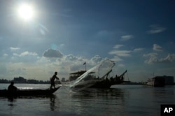 FILE - A fisherman casts his net next to a ferry in the Mekong River near Phnom Penh, Cambodia, Dec. 1, 2015.
