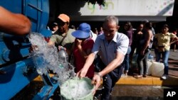 People collect water from a truck that delivers water during rolling blackouts, in Caracas, Venezuela, March 12, 2019.