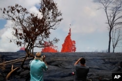 Heath Dalton, right, and Jim Carpenter take pictures as fissures spew lava in the Leilani Estates subdivision near Pahoa, Hawaii, May 22, 2018. Authorities were able to close off production wells at a geothermal plant threatened by a lava flow from Kilauea.