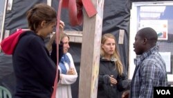 Nigerian Zimako Jones (R), who founded a migrant school at the Jungle camp, talks with volunteer teachers. (L. Bryant/VOA)
