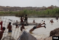 As temperatures soar well past 40 C (104 F) almost every day, children in this camp rip open a fence to swim in a nearby stream in Hassan Sham, Iraqi Kurdistan, May 29, 2018. (H. Murdock/VOA)