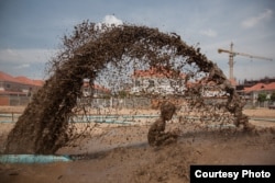 ២៧ មិនា ២០០៩ ភ្នំពេញ កម្ពុជា៖ កុមារ​ម្នាក់ក្នុង​ទឹក​ភក់​ដែល​ត្រូវ​បាញ់​ចេញ​ពីបំពង់​បែក​មួយ ដែល​ជា​ផ្នែក​នៃ​បំពង់​បូម​ខ្សាច់​ចូល​បឹង​ធម្មជាតិ​បឹងកក់​នៅ​ឯ​សហគមន៍​បូរី​រីករាយ។ © Nicolas Axelrod / Ruom