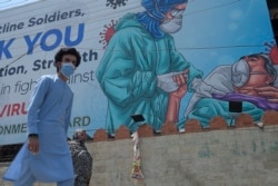 People walk under a billboard that shows gratitude to frontline workers fighting against the spread of the COVID-19 coronavirus, in Rawalpindi on June 30, 2020. (