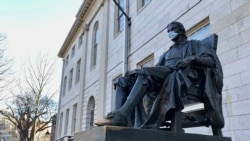 The John Harvard statue at Harvard University, a popular tourist attraction at the campus in Cambridge, Mass, sits adorned with a medical mask as students prepared to leave campus, Saturday, March 14, 2020.