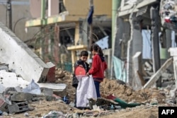 Watoto wa Kipalestina wakisimama katikati ya kifusi cha jengo huko katika kambi ya wakimbizi wa Kipalestina ya Maghazi lililo haribiwa vibaya sana na shambulizi la Israel katika mgogoro unaoendelea kati ya Israel na kikundi cha wanamgambo wa Palestina, Hamas.