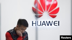 FILE - A staff member stands in front of a Huawei shop in Beijing, China, March 7, 2019. 