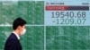 Un transeúnte usando una máscara tras el brote de coronavirus pasa frente a un cartel electrónico que muestra los índices accionarios de Asia en Tokio, Japón, el lunes, 9 de marzo de 2020.