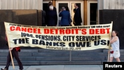 Protesters carry a banner calling for Detroit's debt to be cancelled as people enter the federal courthouse for day one of Detroit's municipal bankruptcy hearings in Detroit, Michigan July 24, 2013. 