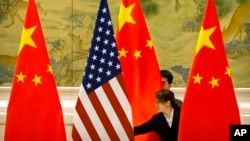 FILE - Chinese staffers adjust U.S. and Chinese flags before a session of negotiations between U.S. and Chinese trade representatives, at the Diaoyutai State Guesthouse, in Beijing, China, Feb. 14, 2019.