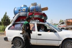 A policeman stands guard at a road checkpoint as an internally displaced family flees from the ongoing fighting between Afghan security forces and Taliban fighters, on the outskirts of Lashkar Gah, the capital city of Helmand province, May 5, 2021.