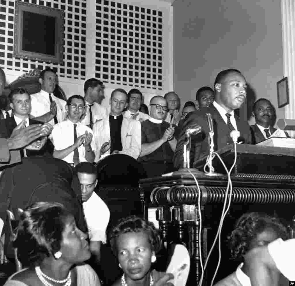 1962 - Wasu malaman addini daga jihohin arewa su na tafa ma shugaban majalisar shugabannin coci-coci na jihohin kudu,m Martin Luther King Jr. a lokacin da yake jawabi cikin wata majami'a a Albany, Jihar Georgia a ranar 28 Agusta, 1962.