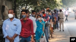 In this Nov. 6, 2020, file photo, people queue to get tested for COVID-19 as a thick quilt of smog lingers over New Delhi, India. (AP Photo/Manish Swarup, File)