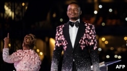 FILE - Pastor Shepherd Bushiri, right, from the Enlightened Christian Gathering stands on stage while his wife speaks to worshippers at the FNB Stadium in Soweto, Jan. 1, 2020.