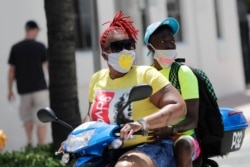 People wearing protective face masks ride a scooter down Ocean Drive during the coronavirus pandemic, Sunday, July 12, 2020, in Miami Beach, Fla.