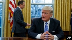 President Donald Trump sits at his desk as he waits for White House Chief of Staff Reince Priebus, left, to deliver three executive orders for his signature, Jan. 23, 2017, in the Oval Office of the White House in Washington.