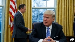 លោក​ប្រធានាធិបតី​ ដូណាល់ ត្រាំ អង្គុយនៅ​តុ​របស់​លោក​នៅ​សេត​វិមាន​ រង់​ចាំ​ប្រធាន​សេតវិមាន​ Reince Priebus ដែល​នៅ​ខាង​ក្រោយ​លោក ដើម្បី​ចុះ​ហត្ថលេខា​លើ​បទ​បញ្ជា​ចំនួន​៣​។