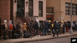 Migrantes hacen fila a la intemperie en el exterior de un centro de ayuda habilitado en la escuela primaria Santa Brígida, el 5 de diciembre de 2023, en Nueva York.