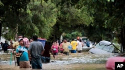 Personas caminan en medio de vehículos abandonados en una calle inundada en Planeta, Honduras el viernes 6 de noviembre de 2020, tras el paso del huracán Eta.