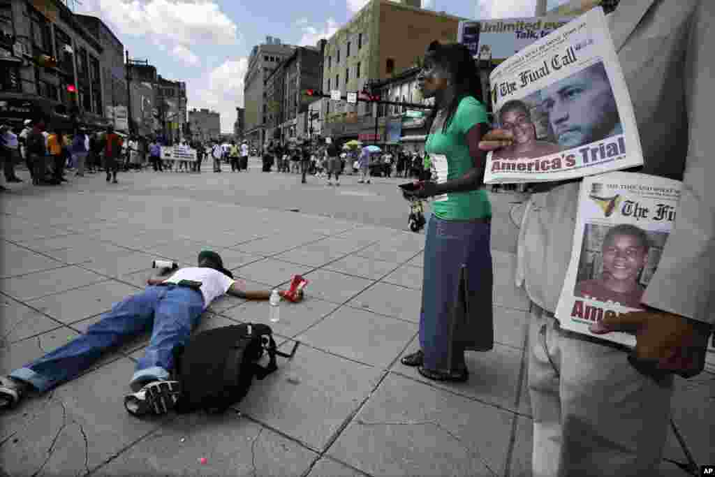 A man holds newspapers as another lies on the street, while a large crowd gathers at an intersection to protest the acquittal of George Zimmerman, Newark, New Jersey, July 14, 2013.