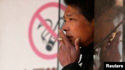 A man smokes in front of a "no smoking" sign outside a shopping mall in Shanghai, January 2014. (REUTERS)