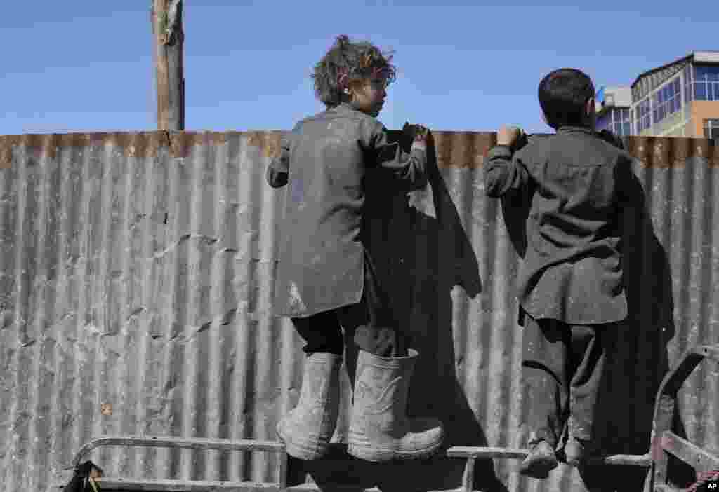 Afghan boys look over a metal barrier at people receiving food supplies during a distribution of humanitarian aid for families in need, in Kabul, Afghanistan.